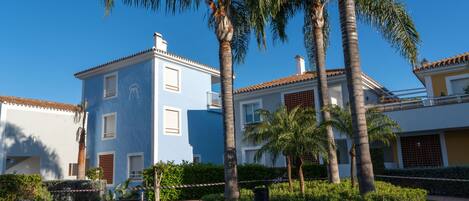 Un edificio de dos plantas con fachada azul, rodeado de palmeras y un césped cuidado.