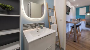 Un baño moderno con un lavabo blanco, un espejo con luz y una escalera de madera apoyada en la pared.