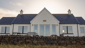 A two-story house with a stone wall in front, a bench, and a small table. - solas Alainn by Interhome (North Skye)