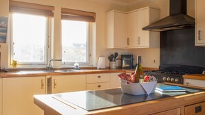 A kitchen with a central island, wooden cabinets, a black range hood, and a window with blinds. - solas Alainn by Interhome (North Skye)