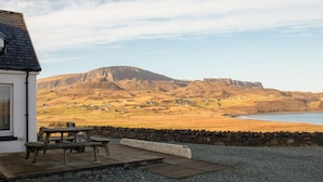 A stone wall and a wooden bench in a gravel area with a view of a mountain and a lake. - solas Alainn by Interhome (North Skye)