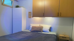 Een slaapkamer met een bed, nachtkastje, houten kledingkast en een klein raam.