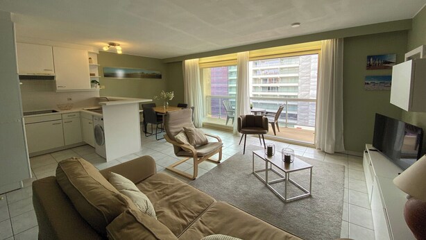 Een ruimtelijke leefruimte met een kitchenette, een bank, een eethoek en een balkon met uitzicht.