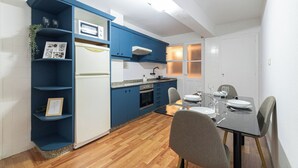 Une cuisine compacte avec des meubles bleus, un réfrigérateur blanc et un coin repas avec une table dressée pour deux personnes.