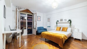 Une chambre à coucher comprenant un lit, un bureau, une chaise, une table de chevet et une porte donnant sur un balcon.