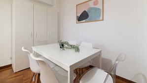 Une table à manger blanche avec des chaises, une plante en pot et un tableau abstrait accroché au mur.