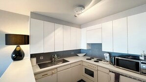 A modern kitchen with white cabinets, a black stove, a microwave, and a sink.