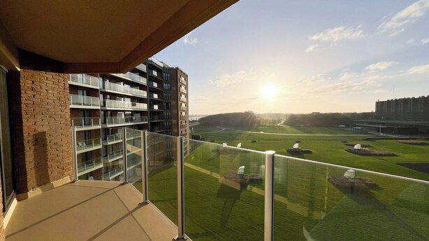 A balcony with a view of a grassy field and a modern building with multiple balconies.
