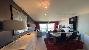 A modern living room with a dining area, a large window, and a red rug.