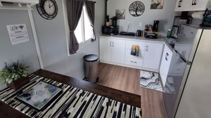 A compact kitchen with white cabinets, a microwave, and a refrigerator. There's a clock on the wall and a sign that reads "PEACOCK".