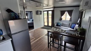 A compact kitchen with a refrigerator, a dining table with chairs, and a sofa in the adjacent living area.