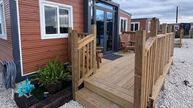 A modern mobile home with a wooden deck, a small garden area, and a clear sky.