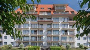 Un immeuble résidentiel à plusieurs étages, doté de balcons, d’une entrée principale et d’un espace de stationnement.