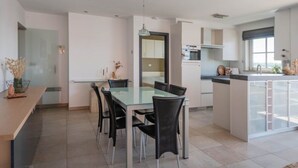 Une cuisine moderne avec une table à manger en verre, des chaises noires et un four encastré.