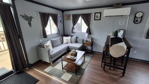 A modern living room with a grey sofa, a wooden coffee table, and a dining area with a chair and table.