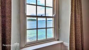 A window with a view of a body of water and a distant landmass. - Cottage in Kingsand by Stunning Beach Views (Cawsand)