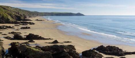 A coastal beach with rocky outcrops and a clear sky.