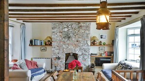 A cozy living room with a stone fireplace, wooden furniture, and a bookshelf. - Cottage in Kingsand by Stunning Beach Views (Cawsand)