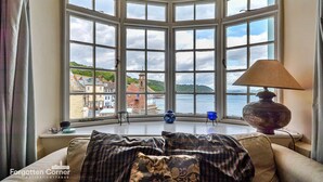 A room with a bay window overlooking a body of water and buildings. - Cottage in Kingsand by Stunning Beach Views (Cawsand)