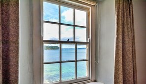 A window with a view of a body of water and a distant landmass. - Cottage in Kingsand by Stunning Beach Views (Cawsand)