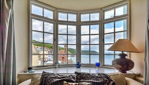 A room with a bay window overlooking a body of water and buildings. - Cottage in Kingsand by Stunning Beach Views (Cawsand)