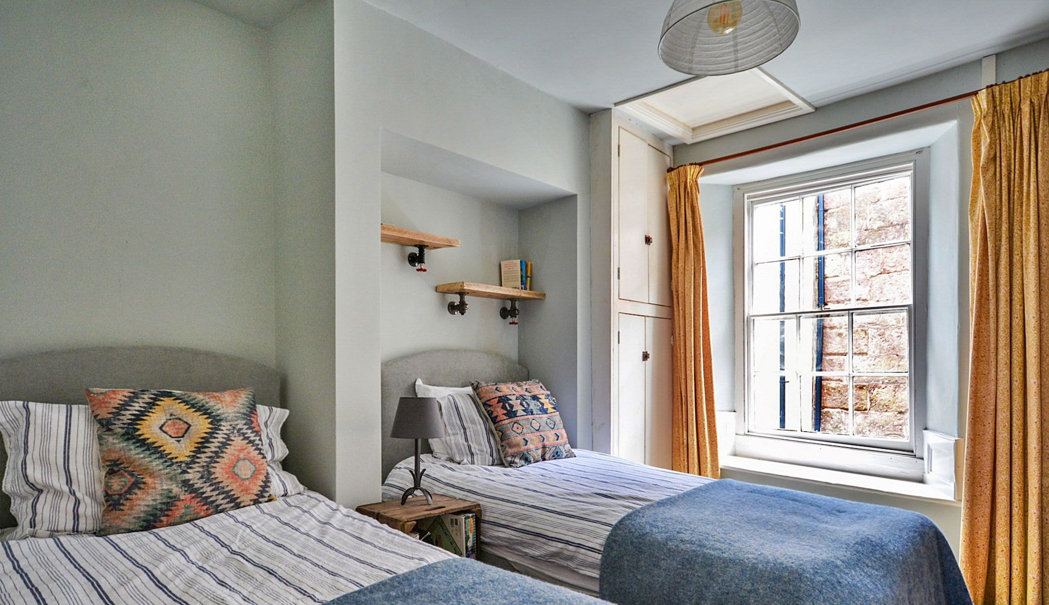 Een slaapkamer met twee bedden, een raam met gordijnen en een plank met boeken.