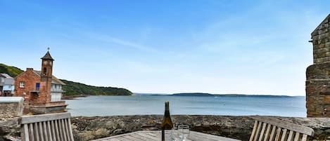 Una mesa de madera con una botella y vasos, con vista al mar tranquilo y una isla distante.