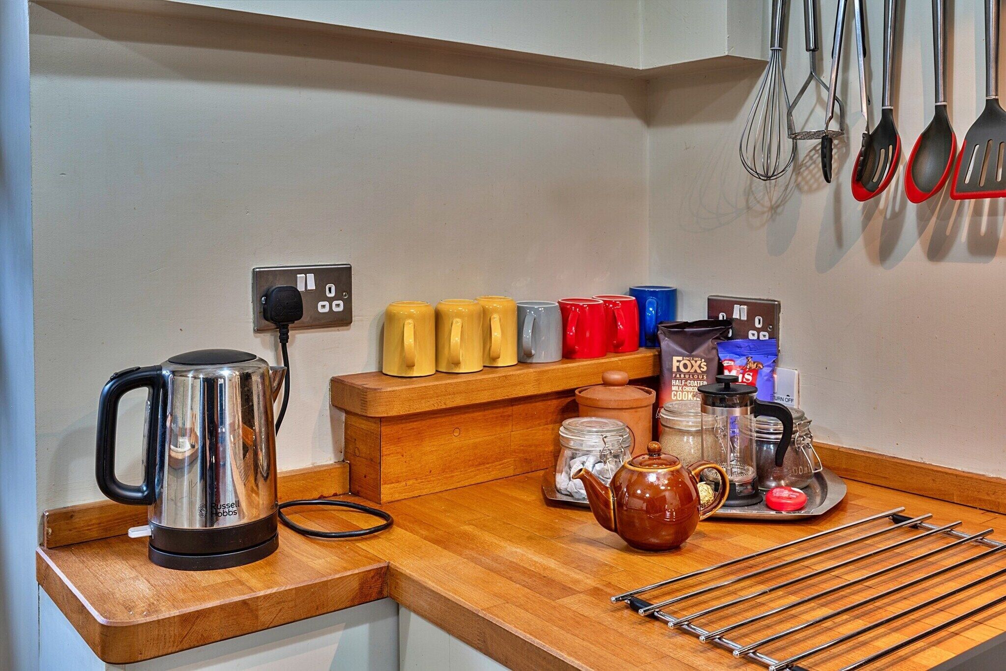 Een keukentafel met een waterkoker, mokken, een theepot en kookgerei.