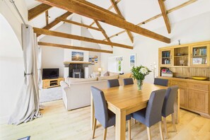Relax in this spacious living area with a high ceiling, dining table for six, comfortable sofa, and modern kitchen.