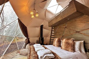 A cozy tent-style room with a bed, a fireplace, and a view of trees outside.