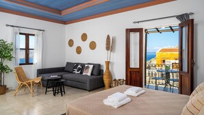 Une pi èce comprenant un lit, un canapé, une petite table et une chaise. Il y a une fenêtre avec des rideaux, une porte donnant sur un espace extérieur et une vue sur la mer.