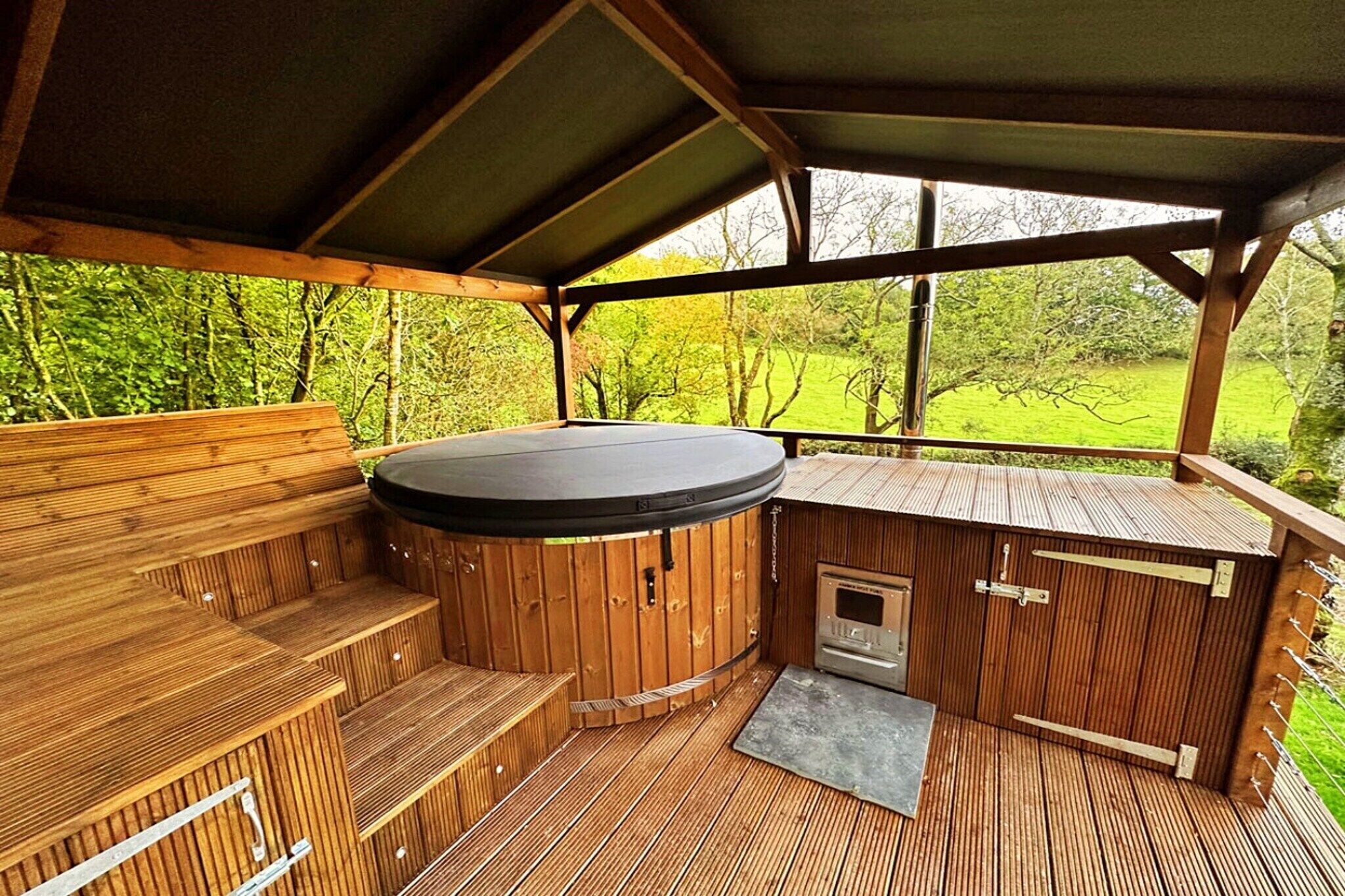 Une terrasse en bois avec un jacuzzi, des bancs en bois et une petite cheminée.