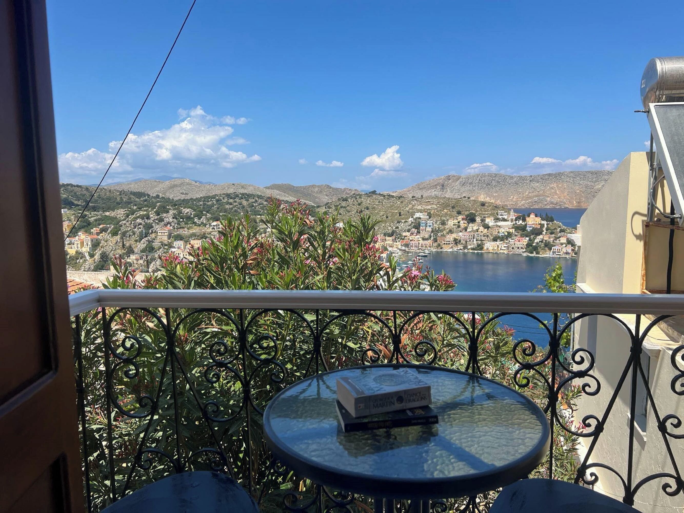 A balcony with a view of a coastal town, a table with books, and a metal railing.