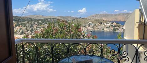 A balcony with a view of a coastal town, a table with books, and a metal railing.