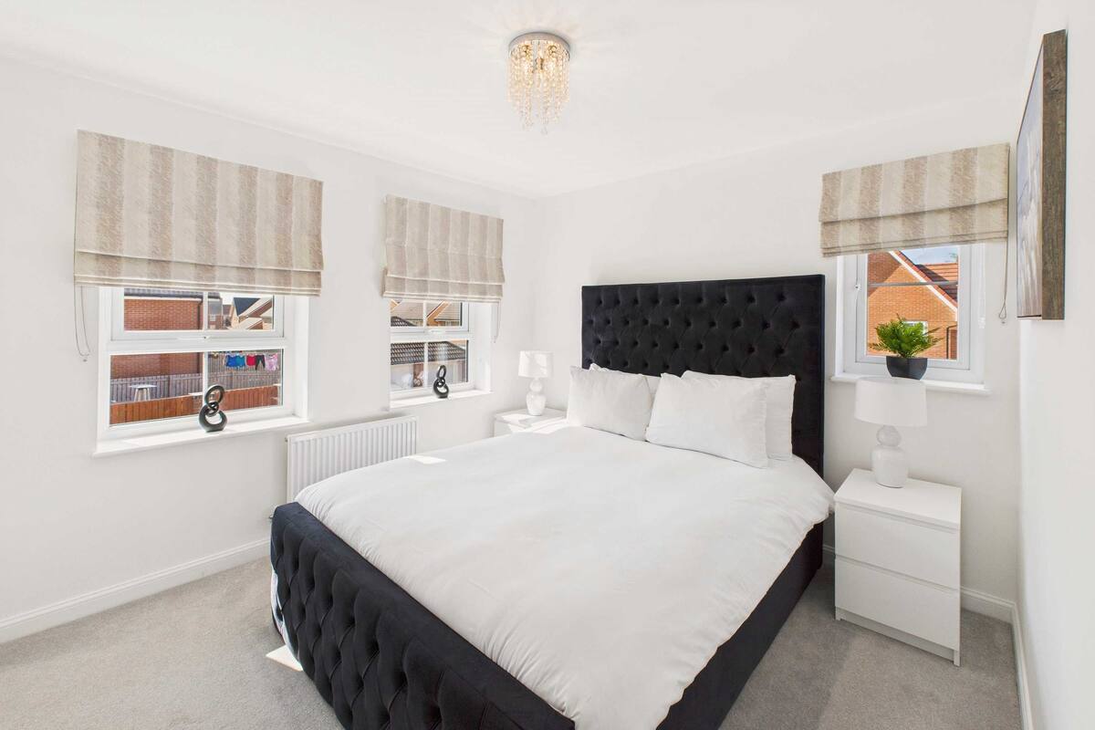 A bedroom with a large bed, white walls, a black headboard, and two bedside tables with lamps.