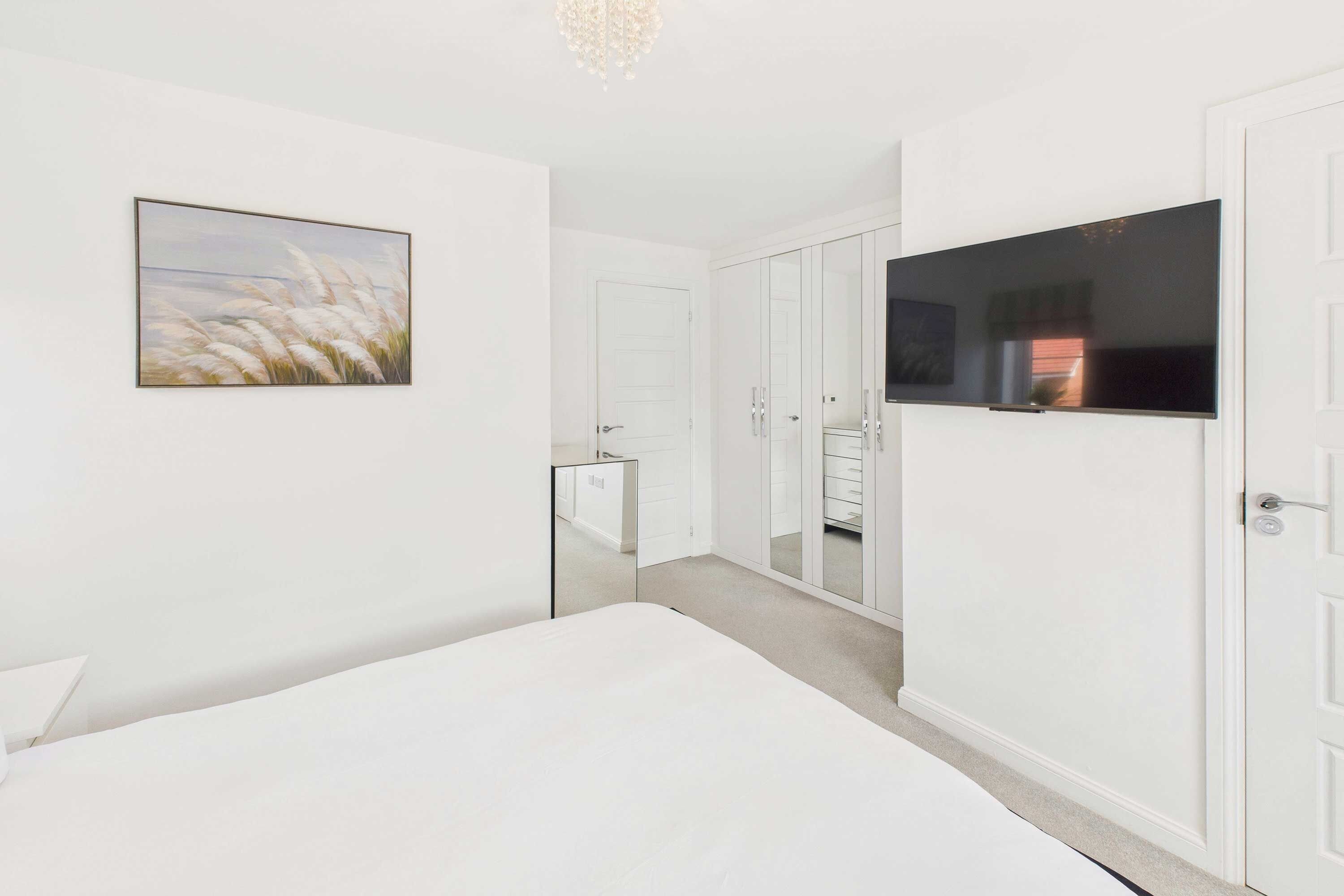 A bedroom with a bed, a television, a wardrobe, and a mirror.