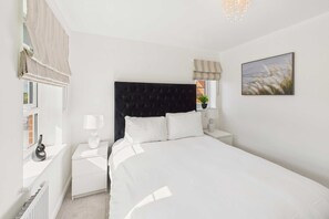 A bedroom with a large bed, white nightstands, a black headboard, a window with curtains, and a painting on the wall. - Host Stay Orient House (Yarm)