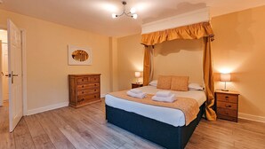 Un dormitorio ordenado con una cama grande, lámparas de noche, un aparador de madera y una puerta que da a otra habitación.