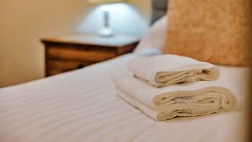 Een opgemaakt bed met witte handdoeken en een bedlampje op een houten nachtkastje.