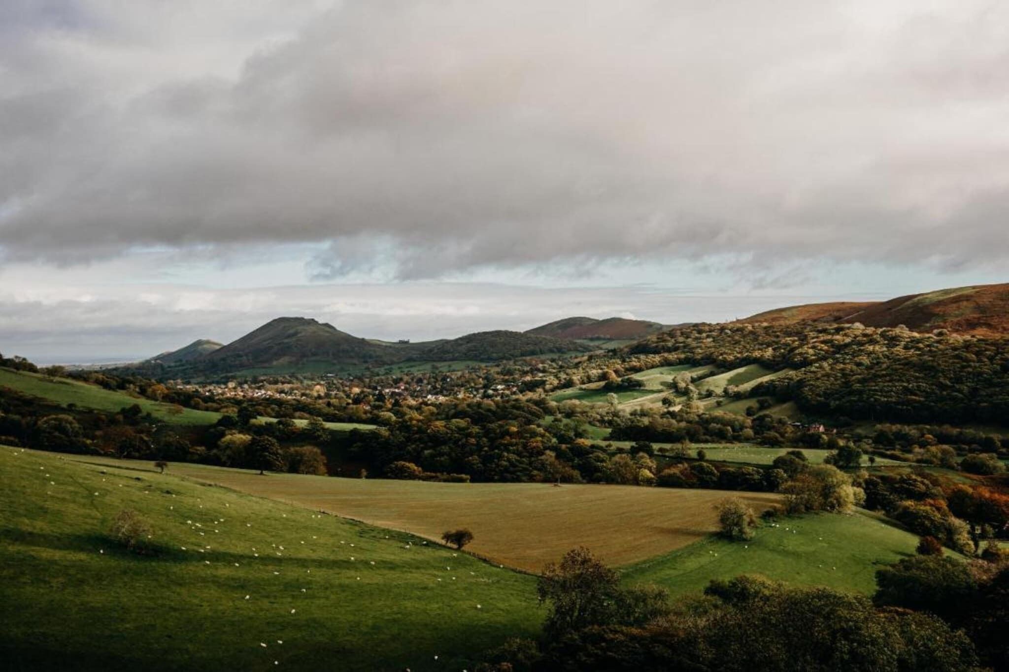 Vista panorámica de un paisaje rural con colinas ondulantes, un pequeño pueblo y una montaña al fondo.
