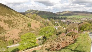 Un paysage rural caractérisé par des collines douces, une route sinueuse et un petit village avec des maisons.