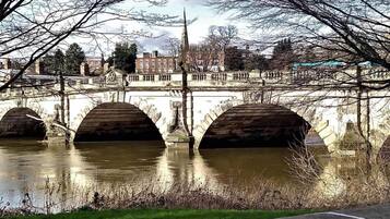 Un pont en pierre, composé de trois arches, enjambe une rivière, et est entouré d’arbres et de bâtiments en arrière-plan.