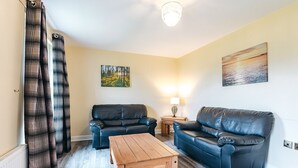 A living room with two black leather sofas, a wooden coffee table, and a lamp on a side table. - 2 bedroom cottage for 4 guests, No Deposit (Dorrington)