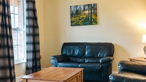 A living room with a black leather sofa, a wooden coffee table, and a painting of a forest on the wall. - 2 bedroom cottage for 4 guests, No Deposit (Dorrington)