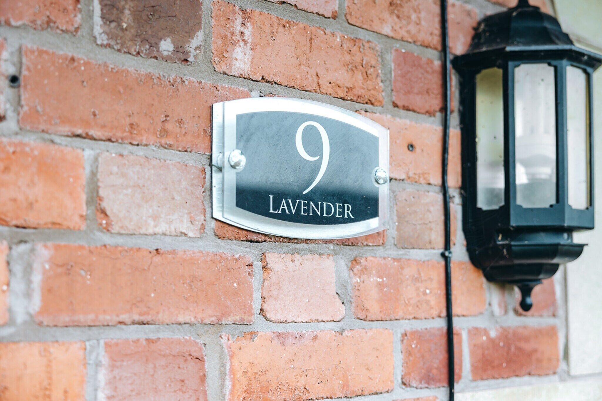 Une plaque indiquant le numéro de la maison, fixée sur un mur de briques, avec une lanterne noire.