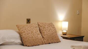 Een net opgemaakt bed met bloemenkussens en een bedlampje.