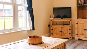 A wooden table with a bowl, a television on a wooden stand, and wooden cabinets in a room with a window. - Cottage in Shropshire near Scenic Trails (Dorrington)