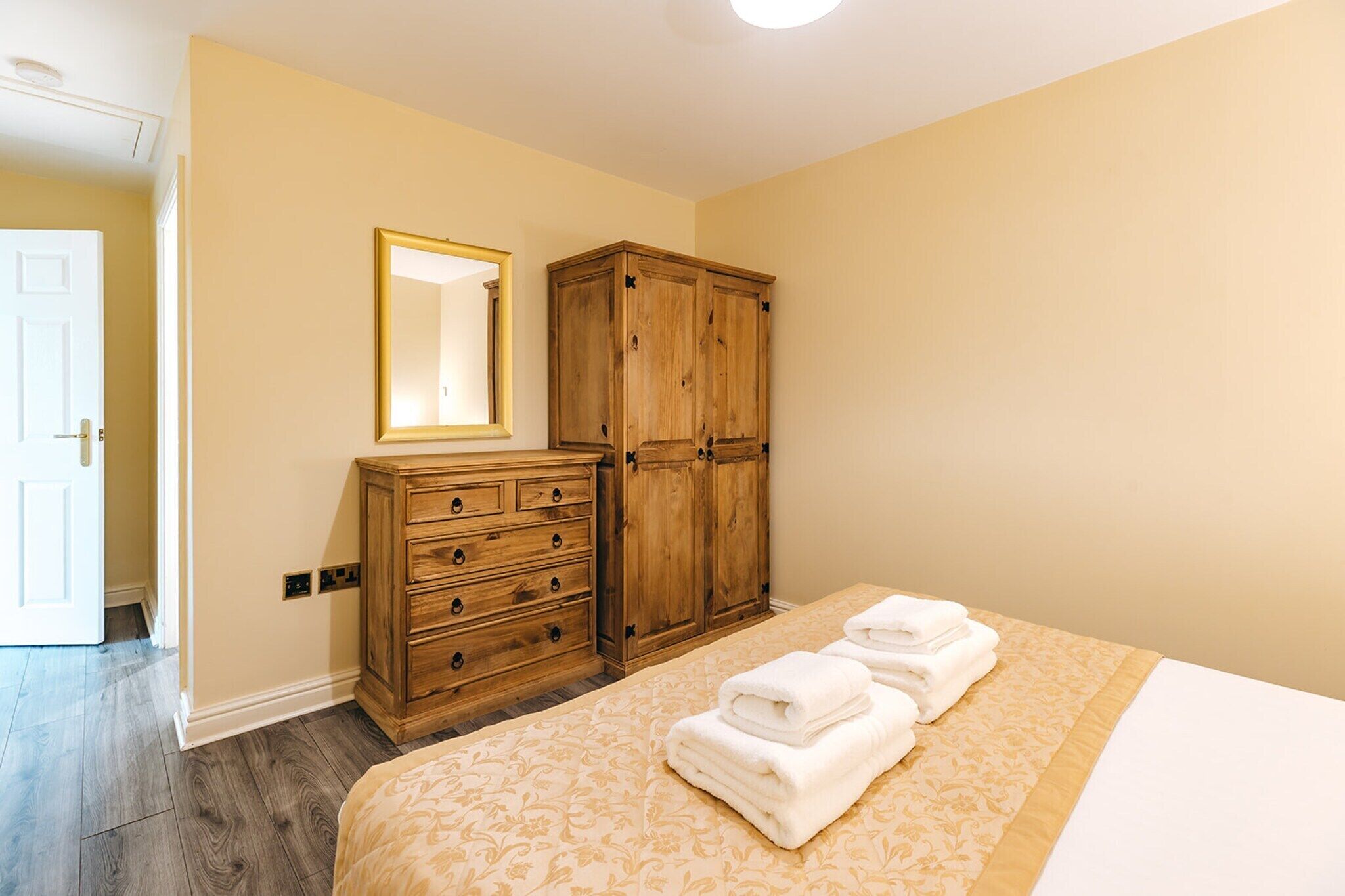 Een slaapkamer met een bed, een houten garderobe, een spiegel en een deur.