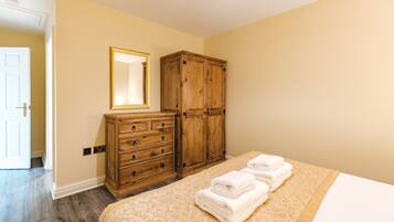 Een slaapkamer met een bed, een houten garderobe, een spiegel en een deur.