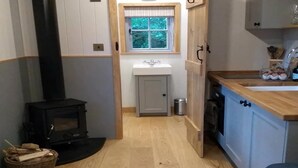 A narrow hallway with a wood-burning stove, a window with a view of greenery, a sink, and a cabinet with a glass container.